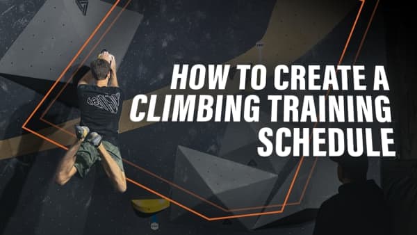 Climber in a black shirt pulls on a hold on an angled bouldering wall, seen from behind