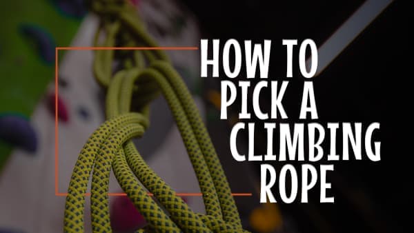 Coiled yellow-green dynamic climbing rope hanging in a gym, with colorful holds blurred in the background
