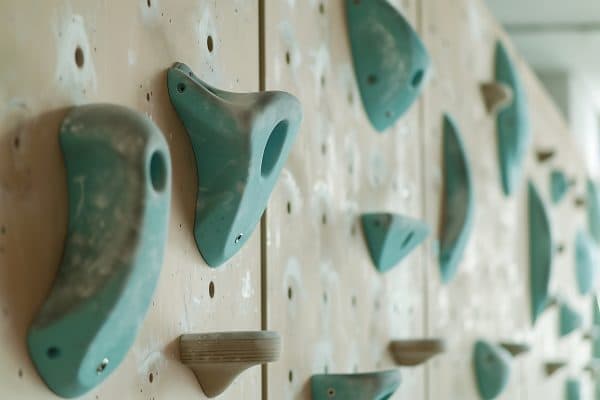Close-up of teal rock climbing holds in various shapes, including pockets and jugs, bolted to a wooden wall