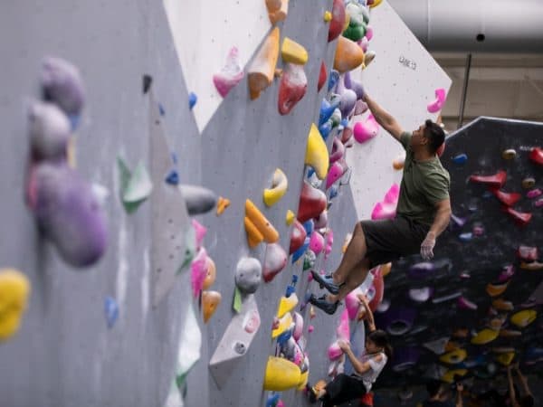 A man in a green shirt leaps for a hold on a climbing wall while a child climbs below