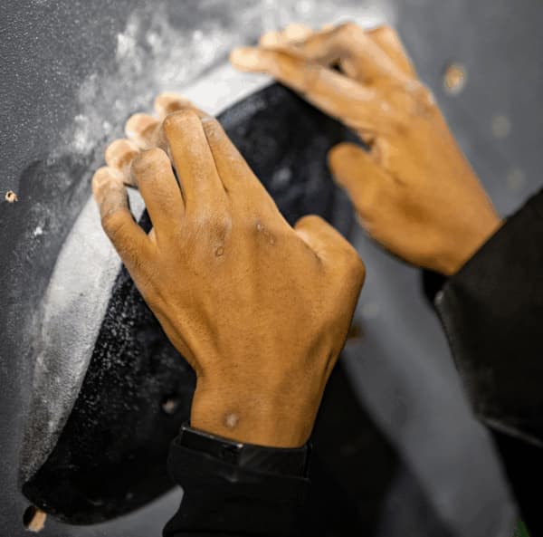 Chalky hands gripping the edge of a large dark hold on a climbing wall