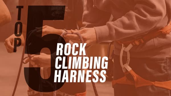 Close-up of climbers' hands tying a rope into an orange harness with a carabiner attached