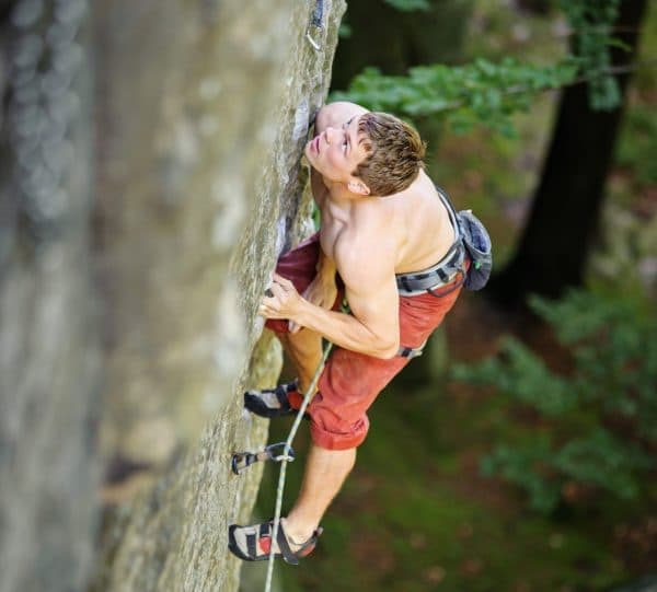 Young athletic man climbing on cliff wall with rope engaged. Outdoor summer day