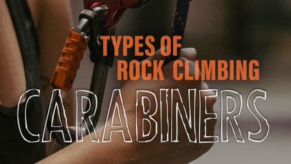 Close-up of a climber's hands clipping a rope into an orange locking carabiner attached to a harness