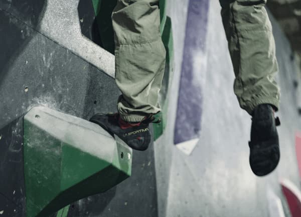 Climber's foot in a La Sportiva shoe edging on a green hold of an indoor bouldering wall
