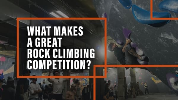 Climber stretches between holds on an indoor bouldering wall while spectators stand watching in the gym below