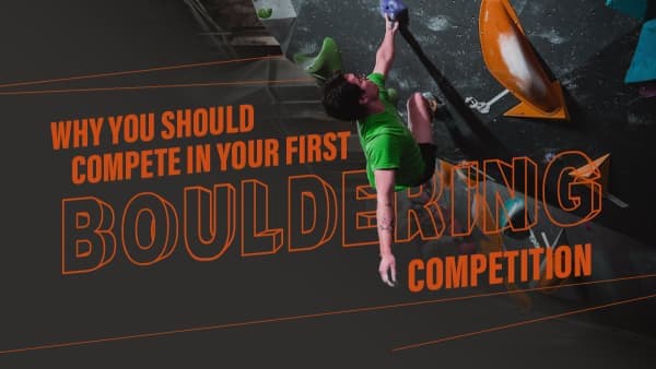 Climber in a green shirt hangs from a high hold on a dark indoor bouldering wall