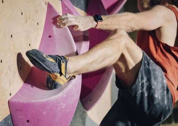 Climber's foot in a gray and yellow climbing shoe pressed against a pink hold on a wall